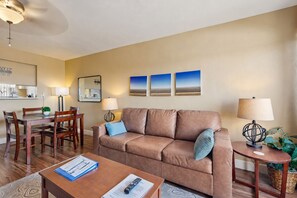 A living room with a brown leather sofa, two side tables with lamps, a wooden dining table with chairs, and a wall-mounted mirror. - Welcoming condo with WiFi & pool - near Scottsdale Fashion Square (Scottsdale)