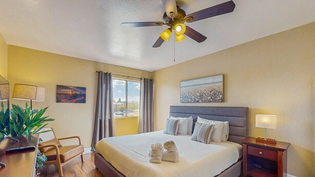 A neatly arranged hotel room with a large bed, a desk with a lamp, a ceiling fan, and a window with curtains. - Welcoming condo with WiFi & pool - near Scottsdale Fashion Square (Scottsdale)
