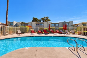 A swimming pool with lounge chairs and umbrellas, surrounded by a fence and buildings. - Welcoming condo with WiFi & pool - near Scottsdale Fashion Square (Scottsdale)