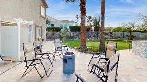An outdoor patio with seating and a fire pit, surrounded by palm trees and a well-maintained lawn. - Luxury home w/ private pool & optional pool heat, rooftop patio & mountain views (Fountain Hills)