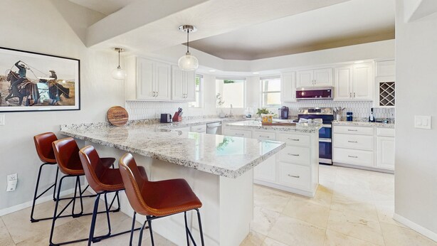 A spacious kitchen with white cabinetry, a large island with bar stools, and modern appliances. - Luxury home w/ private pool & optional pool heat, rooftop patio & mountain views (Fountain Hills)