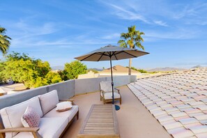 Une terrasse sur le toit, avec un canapé, des chaises et un parasol.