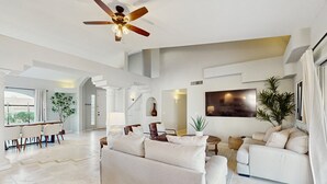 A spacious living room with a ceiling fan, a dining area with a table and chairs, and a large window providing natural light. - Luxury home w/ private pool & optional pool heat, rooftop patio & mountain views (Fountain Hills)