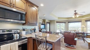 A kitchen with wooden cabinets, a stainless steel microwave, and a gas stove. There is a bar area with a chair and a dining table. - Private Casita Overlooking Winery | Grill, Central AC (Temecula)