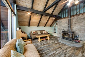 Ein gemütliches Wohnzimmer mit Holzbalkendecke, einem Steinkamin, einer Couch mit Kissen und einem Klavier.