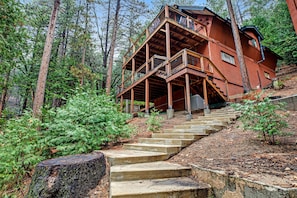 Eine Holzhütte mit einer Treppe, die zu einem Balkon führt, umgeben von einem Wald.