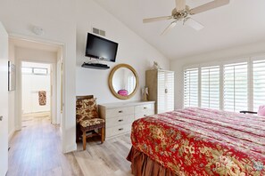 Ein Schlafzimmer mit einem Bett, einem Fernseher, einem Spiegel, einer Kommode und einem Deckenventilator.
