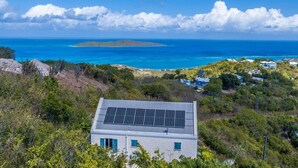 Ein Küstenanwesen mit Solaranlage auf dem Dach, Blick auf den Ozean und einer kleinen Insel in der Ferne.