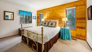 A bedroom with a wooden wall, a bed with a metal frame, two bedside tables, and a window with blinds. - Secluded Dog-Friendly Cabin w/Wood Fireplace, Deck, Private W/D, Mtn Views (Idyllwild)
