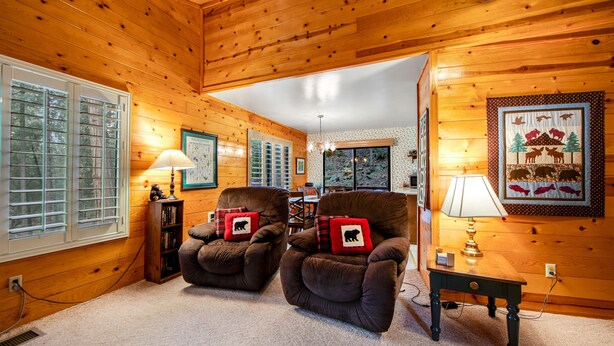 A cozy cabin interior with wooden walls, two armchairs with bear-themed pillows, a table with a lamp, and a framed wildlife scene on the wall. - Secluded Dog-Friendly Cabin w/Wood Fireplace, Deck, Private W/D, Mtn Views (Idyllwild)