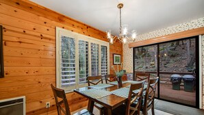 A wooden interior with a dining table, chairs, a chandelier, and a view of the outdoors through a sliding door. - Secluded Dog-Friendly Cabin w/Wood Fireplace, Deck, Private W/D, Mtn Views (Idyllwild)