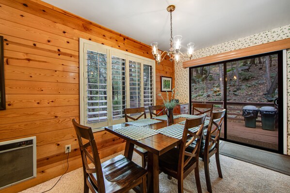 Un intérieur en bois comprenant une table à manger, des chaises, un lustre et une vue sur l’extérieur grâce à une porte coulissante.