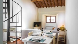 A dining area with a white table set for four, a spiral staircase, and a TV in the background. - Apartment "Il Campo", in the center of Siena, a few steps from Piazza del Campo (siena)