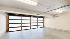 Eine Garage mit großer, offener Tür, Leuchtstofflampen und einem Betonboden.