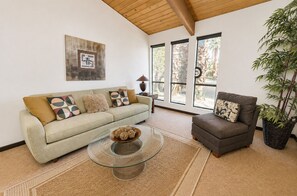 A living room with a sofa, armchair, and coffee table, large windows with a view, and a wall-mounted artwork. - Stylish Mid-century gem near downtown with pool, hot tub, fire table & WiFi (Palm Springs)