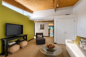 Ein Wohnzimmer mit Flachbildfernseher, einer Couch, einem Sessel, einem Glastisch und einem Kleiderschrank.
