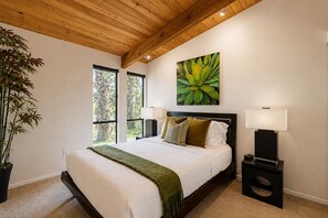 A bedroom with a bed, bedside lamps, a painting, and a large window. - Stylish Mid-century gem near downtown with pool, hot tub, fire table & WiFi (Palm Springs)