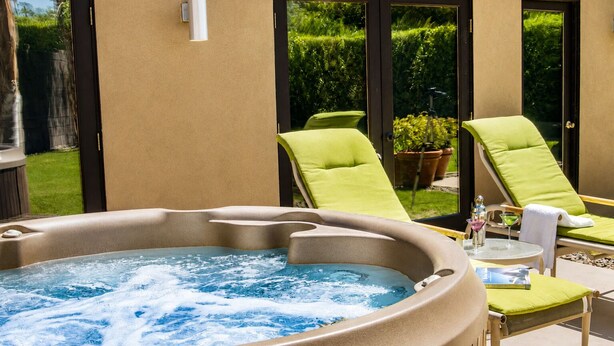 Ein Whirlpool mit Glasverkleidung, umgeben von Liegestühlen und einem kleinen Tisch mit einem Getränk.