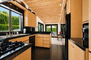 A modern kitchen with wooden cabinets, black countertops, and a central island. - Stylish Mid-century gem near downtown with pool, hot tub, fire table & WiFi (Palm Springs)