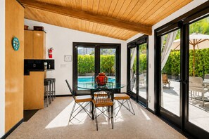 A modern kitchen with wooden cabinets, a glass dining table, and a view of a swimming pool outside. - Stylish Mid-century gem near downtown with pool, hot tub, fire table & WiFi (Palm Springs)