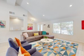 Un salon spacieux avec un grand canapé d’angle, une table basse ronde et un tapis géométrique aux couleurs vives.