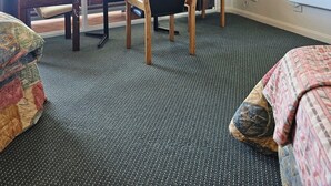 Ett hotellrum med ett stort fönster, en platt-TV som är monterad på väggen, en trästol, ett litet bord och ett mönstrat överkast.