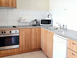 A kitchen with wooden cabinets, a microwave, a coffee maker, and a dishwasher. - Room 20: Spacious 2-BR Central Apartment - 1 Queen & 3 Singles - Full Amenities (Jindabyne)