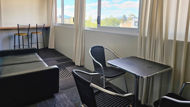 Ett rum med en soffa, två fåtöljer, ett litet bord och ett fönster med gardiner.