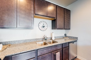 A kitchen with dark wooden cabinets, a granite countertop, a stainless steel sink, and a wall-mounted coffee sign. - Spacious mountain view escape with guest house, patio & washer/dryer - near golf (Flagstaff)