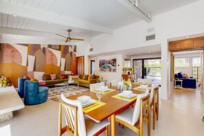 A spacious living room with a large wooden dining table, blue armchairs, and a colorful abstract wall. - Deluxe Vista Las Palmas home w/private pool & spa - close to downtown (Palm Springs)