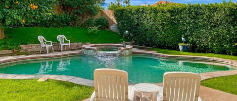 A swimming pool with two white chairs and a small table, surrounded by a well-maintained lawn and hedges.