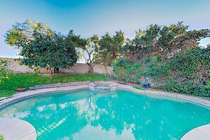 Une piscine à bord incurvé, entourée d’un mur de briques et d’une végétation luxuriante.