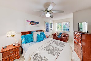 Une chambre à coucher comprenant un lit, un ventilateur de plafond, une commode, un téléviseur et une fenêtre avec des stores.