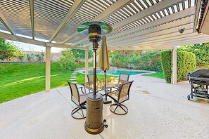 Un patio couvert avec un barbecue, des sièges d’extérieur et une vue sur une cour arrière avec une piscine.