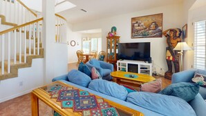 Een ruime woonkamer met een blauwe zithoek, een houten salontafel en een televisie.