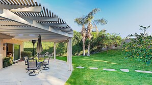 Een overdekt terras met tuinmeubilair, een pergola en een verzorgd gazon met looppadjes.