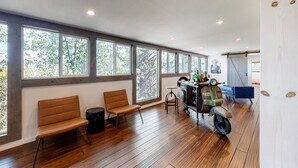 A spacious room with large windows, a wooden floor, and a vintage scooter. - Charming home with full kitchen, fireplace, grill, & viewing deck (Idyllwild)