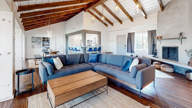 A spacious living room with a large sectional sofa, wooden beams, and a fireplace. - Charming home with full kitchen, fireplace, grill, & viewing deck (Idyllwild)