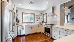 A modern kitchen with stainless steel appliances, wooden flooring, and white cabinetry. - Charming home with full kitchen, fireplace, grill, & viewing deck (Idyllwild)