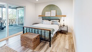 A bedroom with a bed, a bedside table, a lamp, a wicker chest, and a large window with a view of the outdoors. - Charming home with full kitchen, fireplace, grill, & viewing deck (Idyllwild)