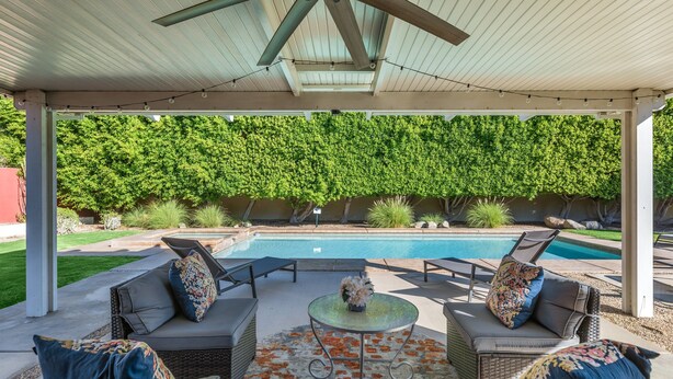 Un espace extérieur aménagé en terrasse, doté d’un coin salon couvert, d’une piscine et d’un décor luxuriant et verdoyant.
