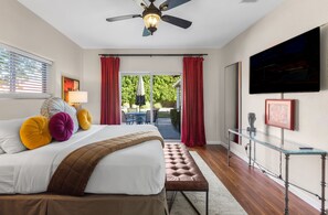Une chambre à coucher avec un lit, un ventilateur de plafond, une télévision et une vue sur l’extérieur.