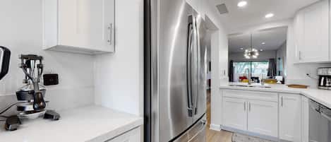 A modern kitchen with stainless steel appliances, white cabinetry, and a wooden floor.