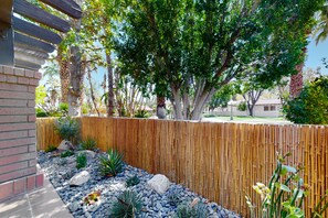 A garden with a wooden fence, a variety of plants, and a stone pathway. - Vibrant dog-friendly condo with hot tub, tennis court, pool, W/D, grill & patio (Palm Springs)