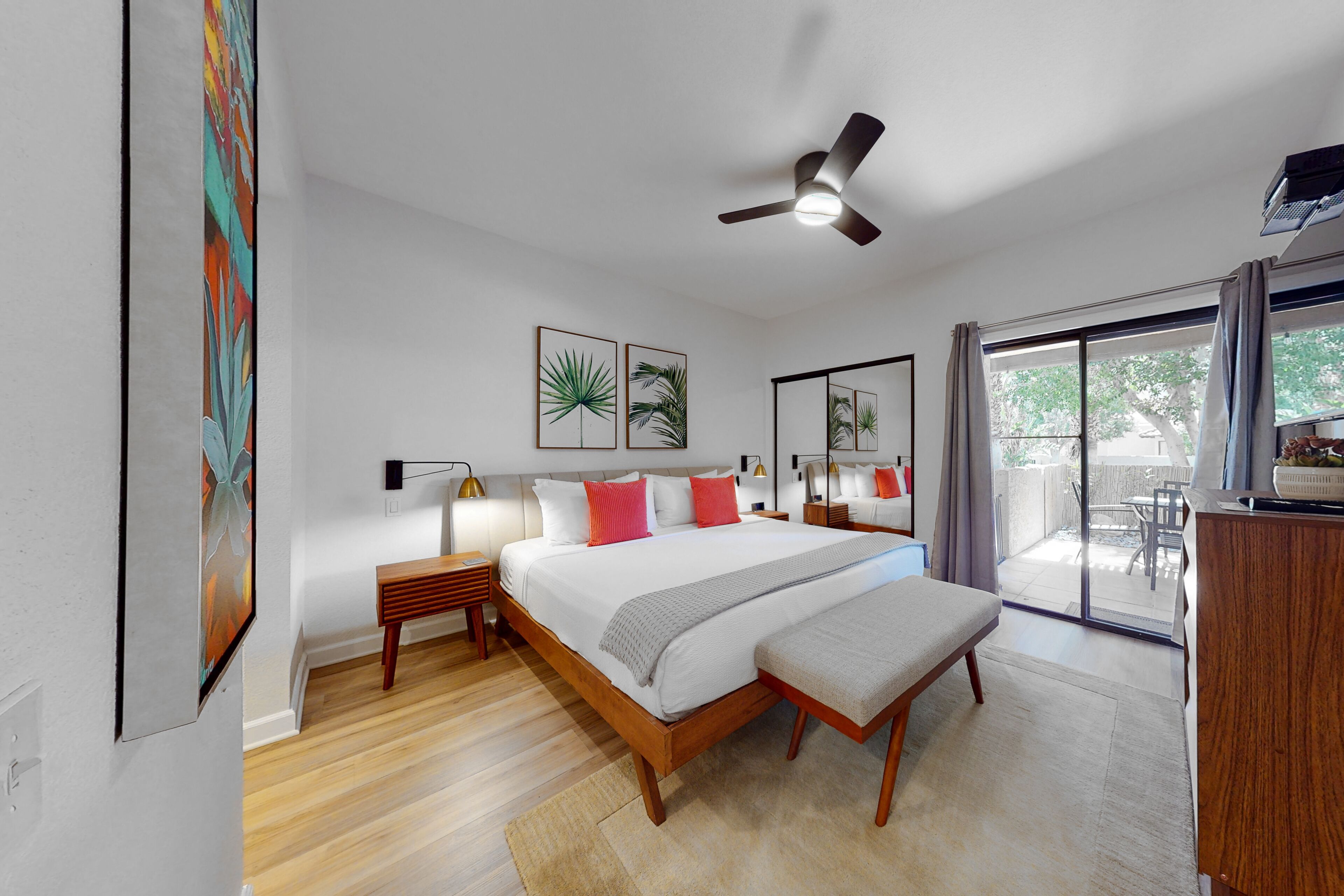A modern bedroom with a large bed, bedside tables, a ceiling fan, and a sliding glass door to a patio.