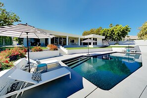 Un área de piscina exterior moderna con piscina azul cristalina, sillones de descanso y sombrillas.