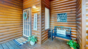 L’entrée d’un chalet en bois, avec un paillasson, un banc et une pancarte indiquant « LIEU DE RASSEMBLEMENT ».