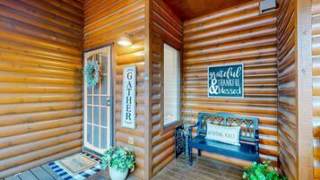 L’entrée d’un chalet en bois, avec un paillasson, un banc et une pancarte indiquant « LIEU DE RASSEMBLEMENT ».