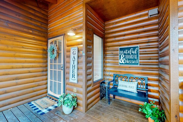 Entrada de una cabaña de madera con un felpudo, un banco y un letrero que dice "GATHERING PLACE".