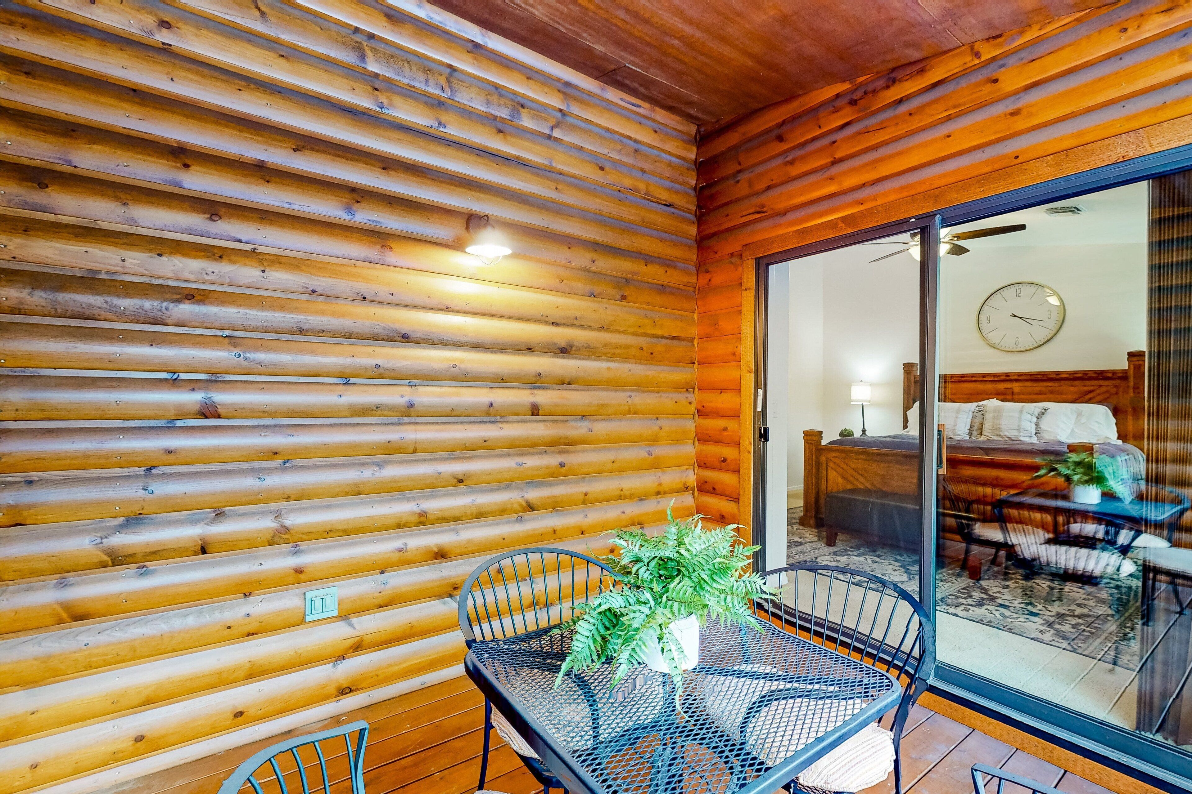 A wooden cabin interior with a dining area, a bed, and a visible clock.